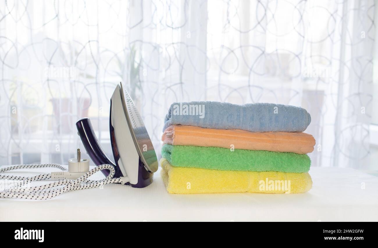 Towels folded in a roll and an iron after ironing on an ironing board. housekeeping concept Stock Photo