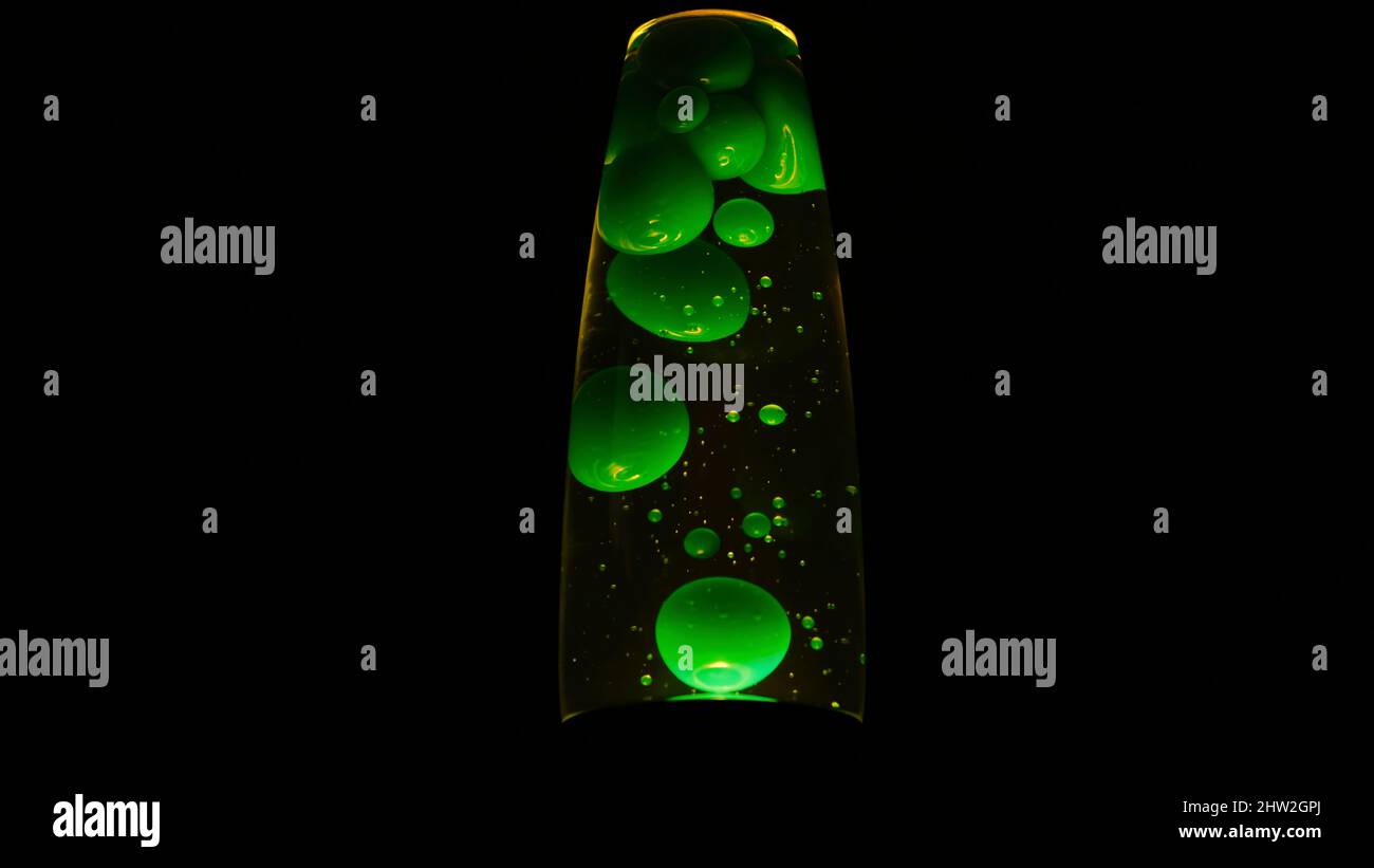 Green lava lamp on black background. Concept. Beautiful neon-lit lava lamp in total darkness. Retro neon night light with moving bubbles. Lava lamp. Stock Photo