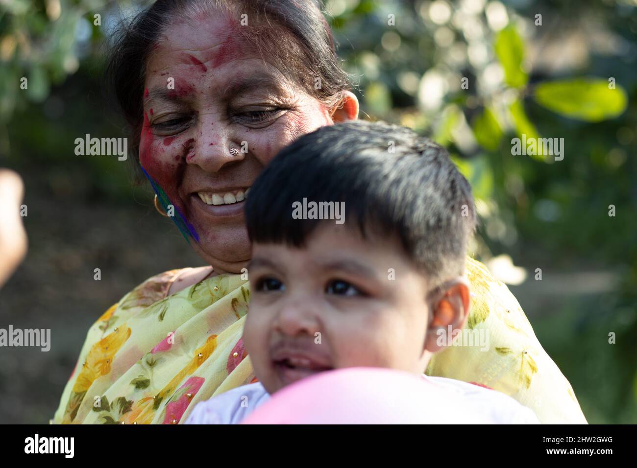 Happy Asian Indian Kid Boy And Grandmother Enjoying The Festival Of Colors With Holi Color Powder Called Gulal Or Rang Stock Photo