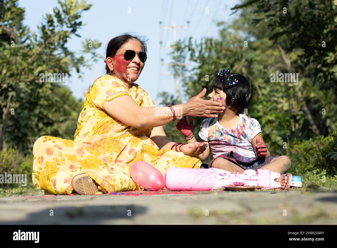 Happy Asian Indian Kid Girl And Grandmother Enjoying The Festival Of Colors With Holi Color Powder Called Gulal Or Rang Stock Photo