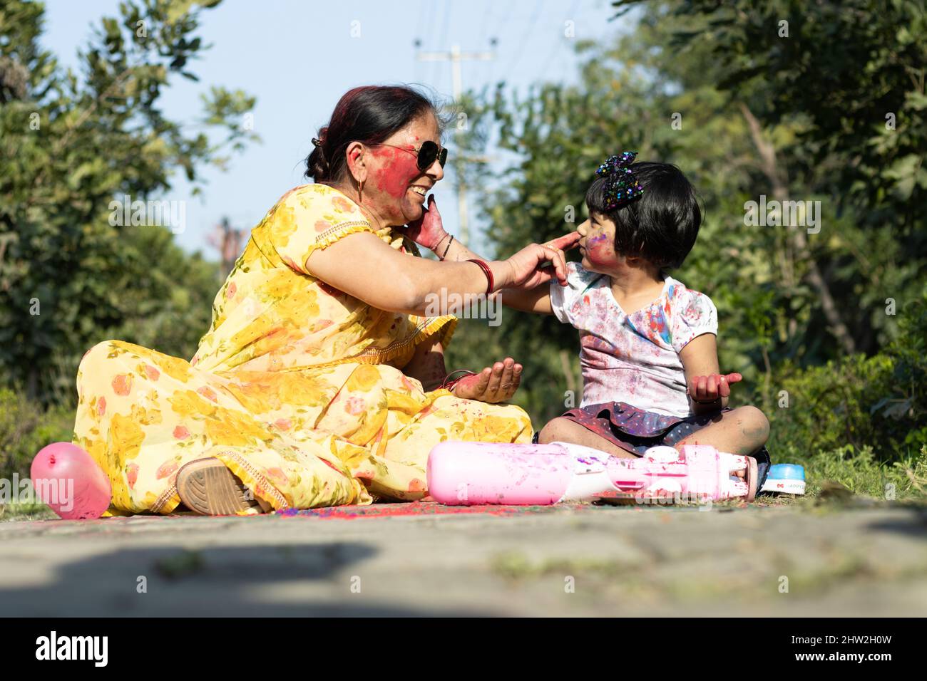 Happy Asian Indian Kid Girl And Grandmother Enjoying The Festival Of Colors With Holi Color Powder Called Gulal Or Rang Stock Photo