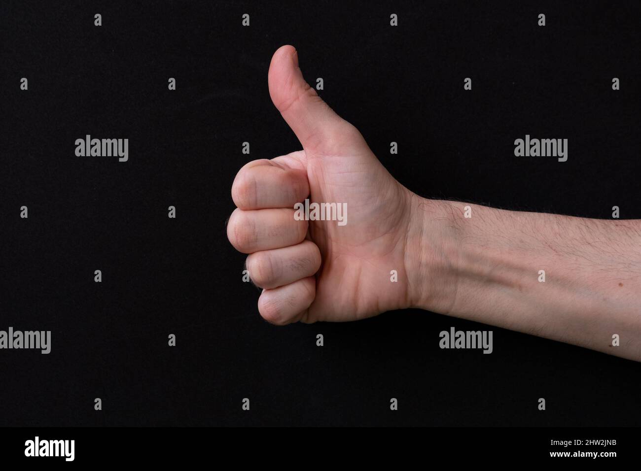 Close-up of man hand showing thumb up, on a black background. Stock Photo