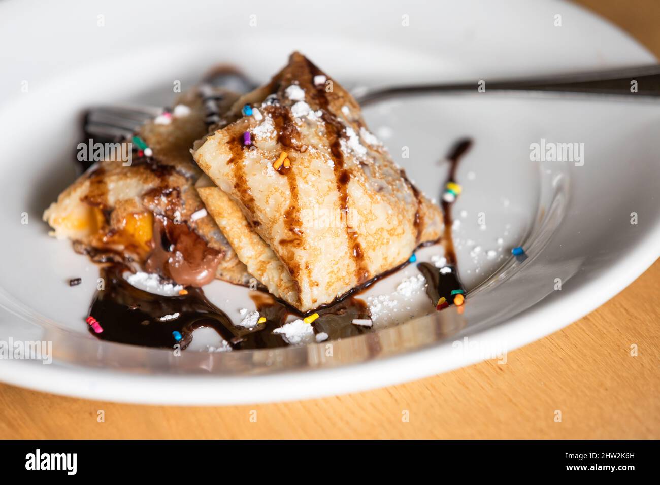 Stuffed sweet crepes with chocolate syrup and candies, close up photo Stock Photo