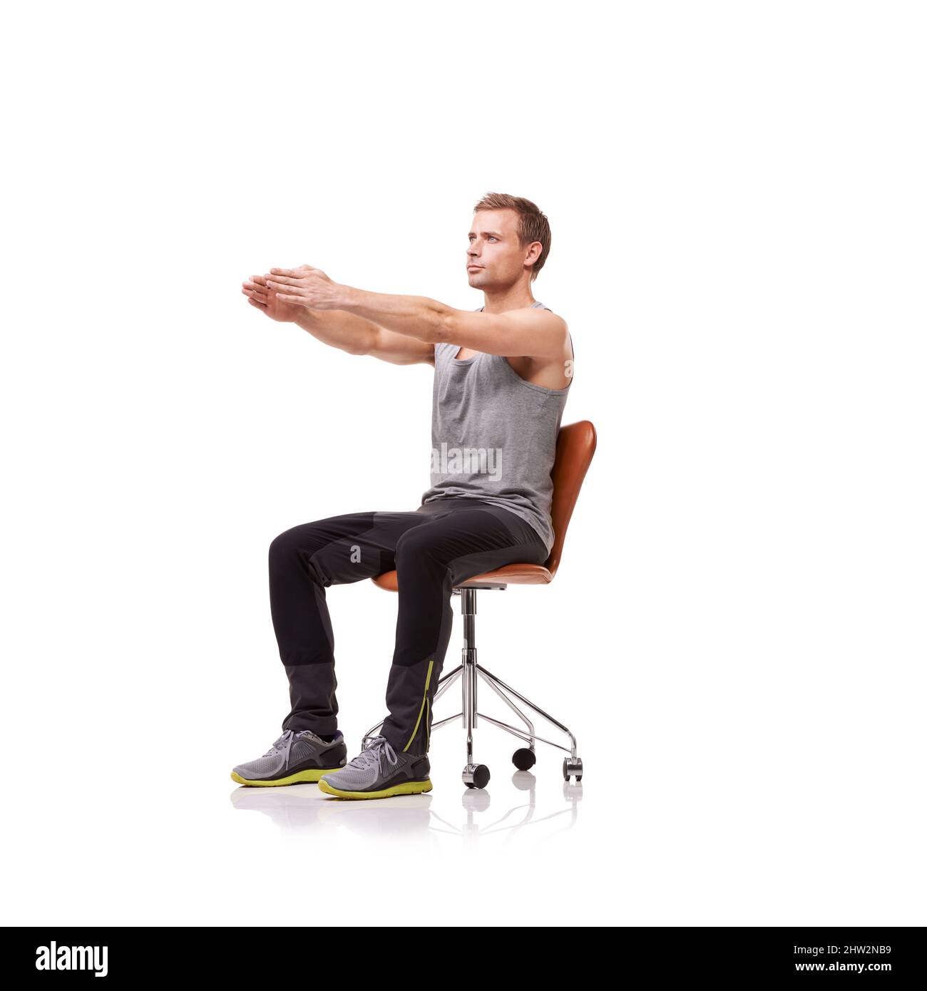 Keeping his limbs long and lean. A handsome young man wearing gym clothes and stretching while seated in an office chair against a white background. Stock Photo
