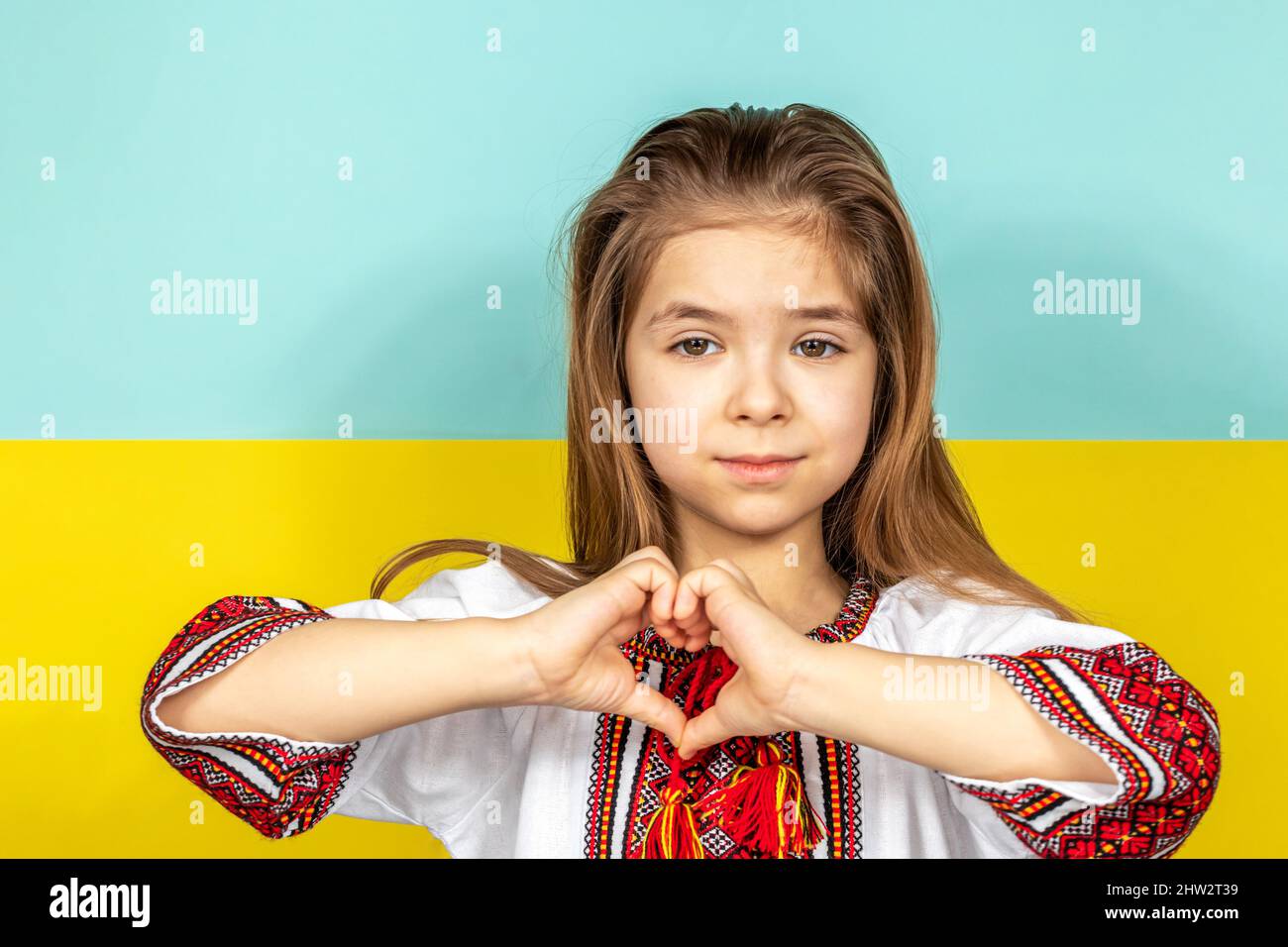 A girl in national Ukrainian clothes, an embroidered shirt, shows a heart sign as a sign of love for Ukraine, close-up against the background of the Stock Photo