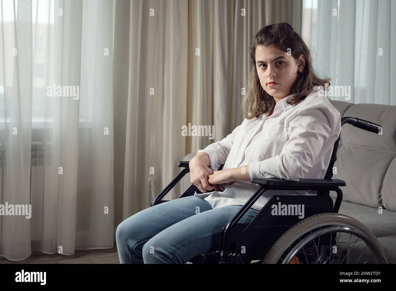 Sad disabled woman in wheelchair looks out of window at home Stock Photo