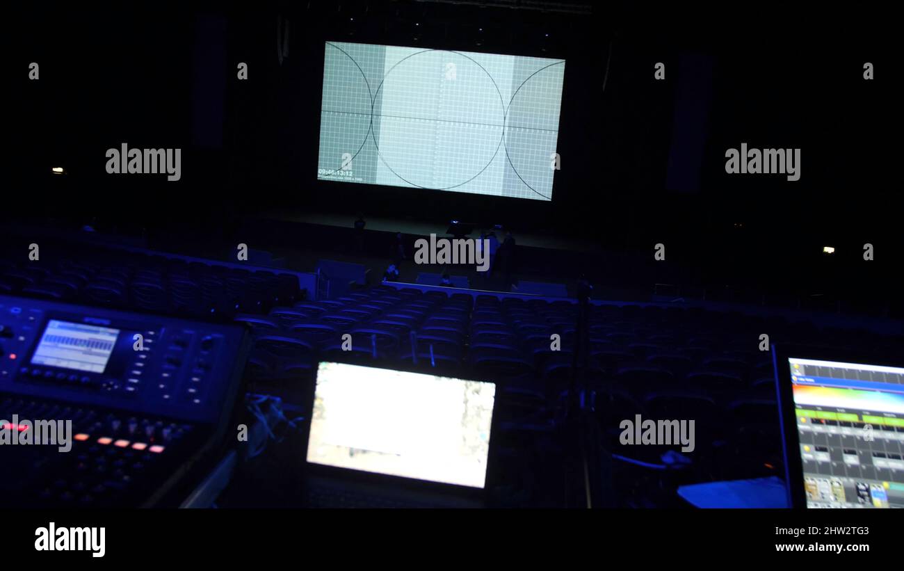 Theatre hall in preparation for show. Professional equipment and laptops glow on table in dark of theater hall on preparation before performance. Stock Photo