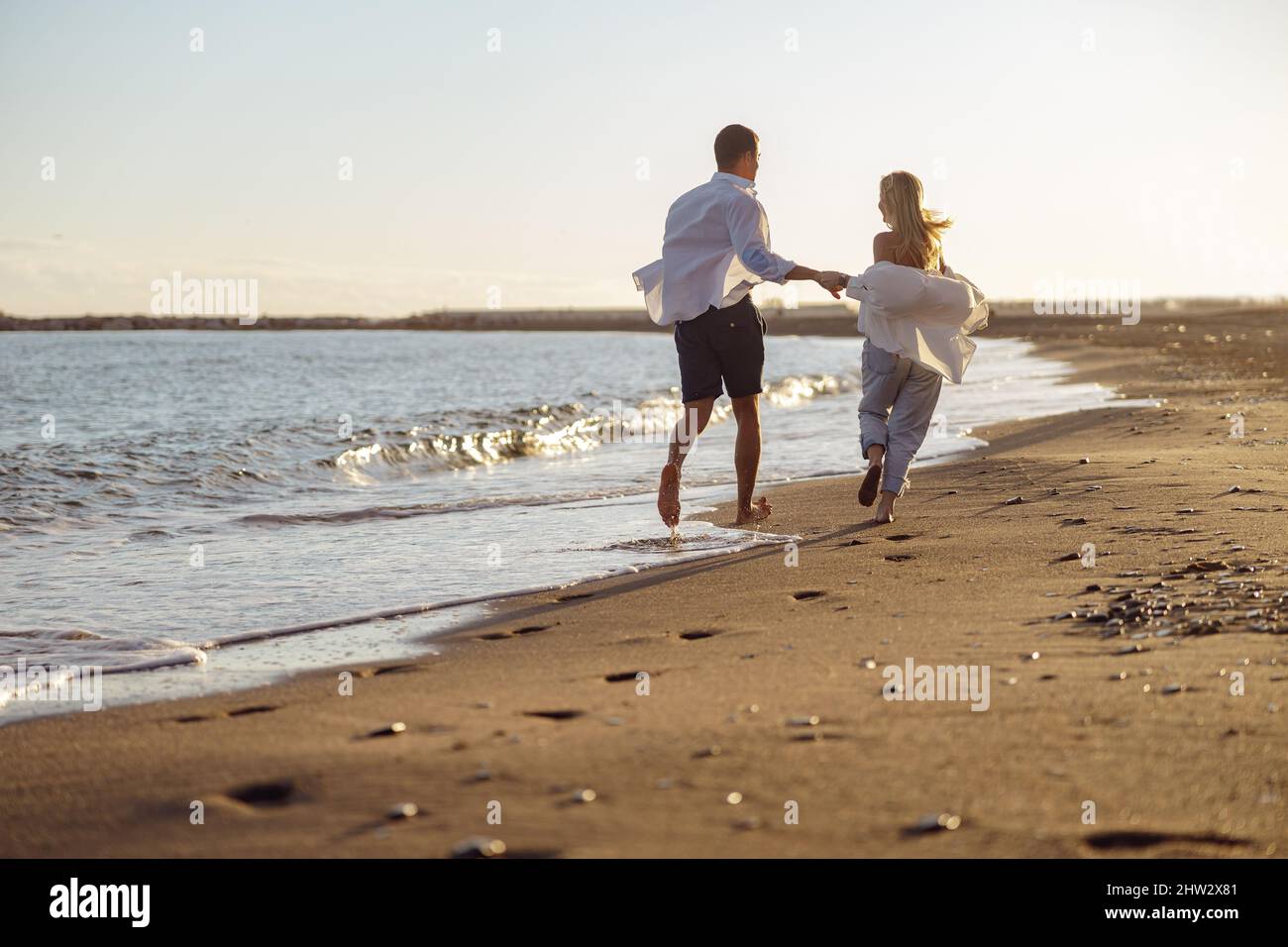 Happy couple running along the beach holding hands Stock Photo
