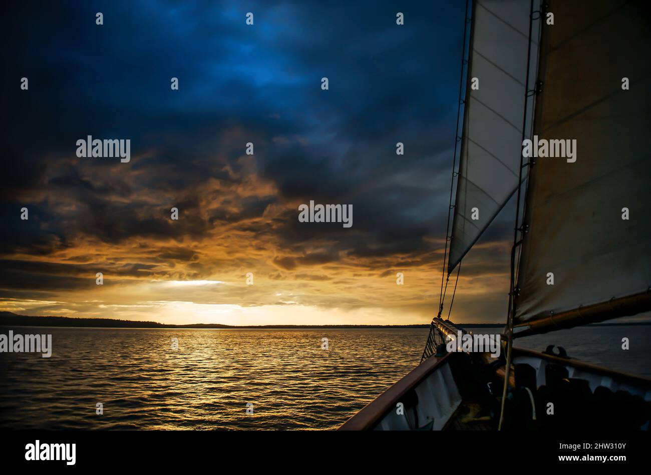 A ship sails towards the sunset below dark ominous clouds Stock Photo