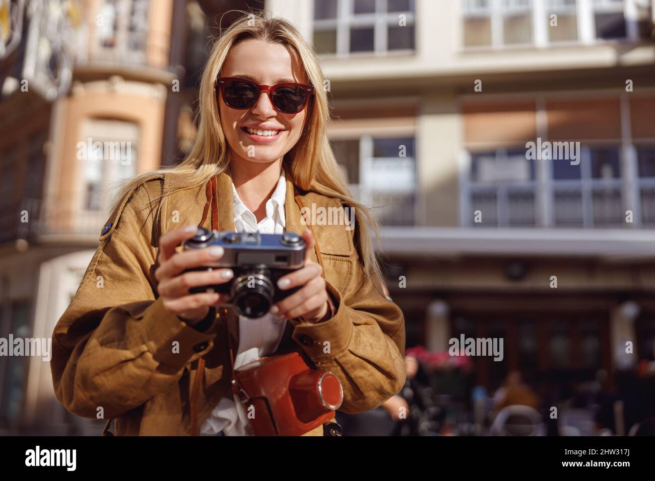 Charming lady standing on street near cafe, holding retro camera Stock Photo