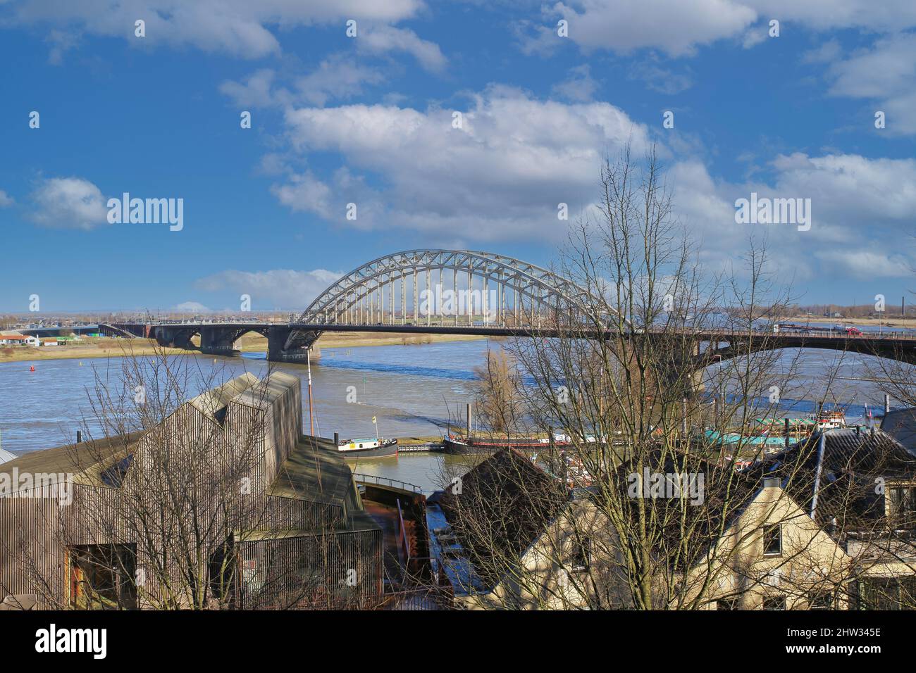 Nijmegen (Waalbrug), Netherlands - February 27. 2022: View fom hill over river waal on steel arch bridge with two pylons against blue winter sky Stock Photo