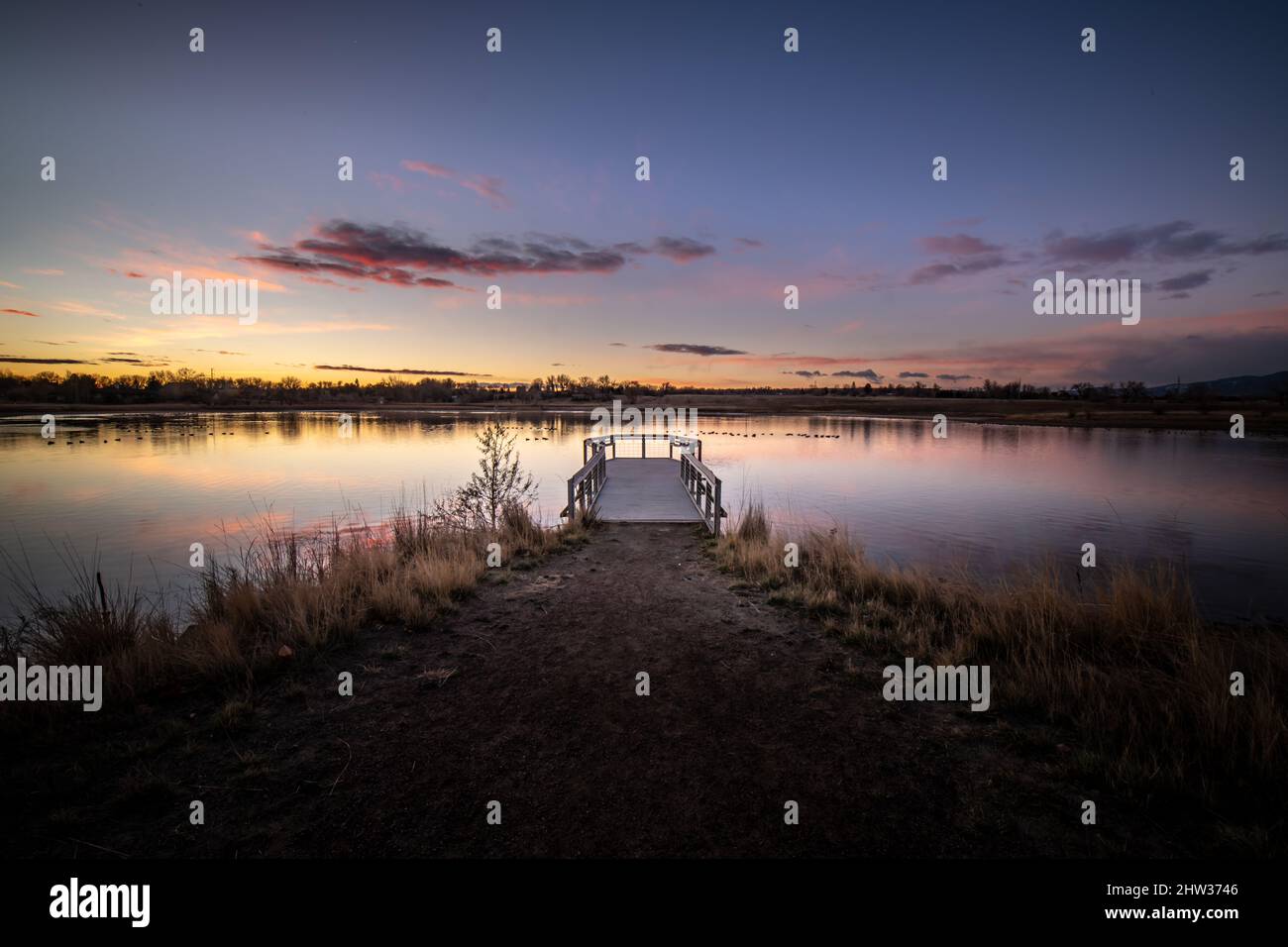 A purple sky just before sunrise over a pond with a pier extending away from the camera Stock Photo