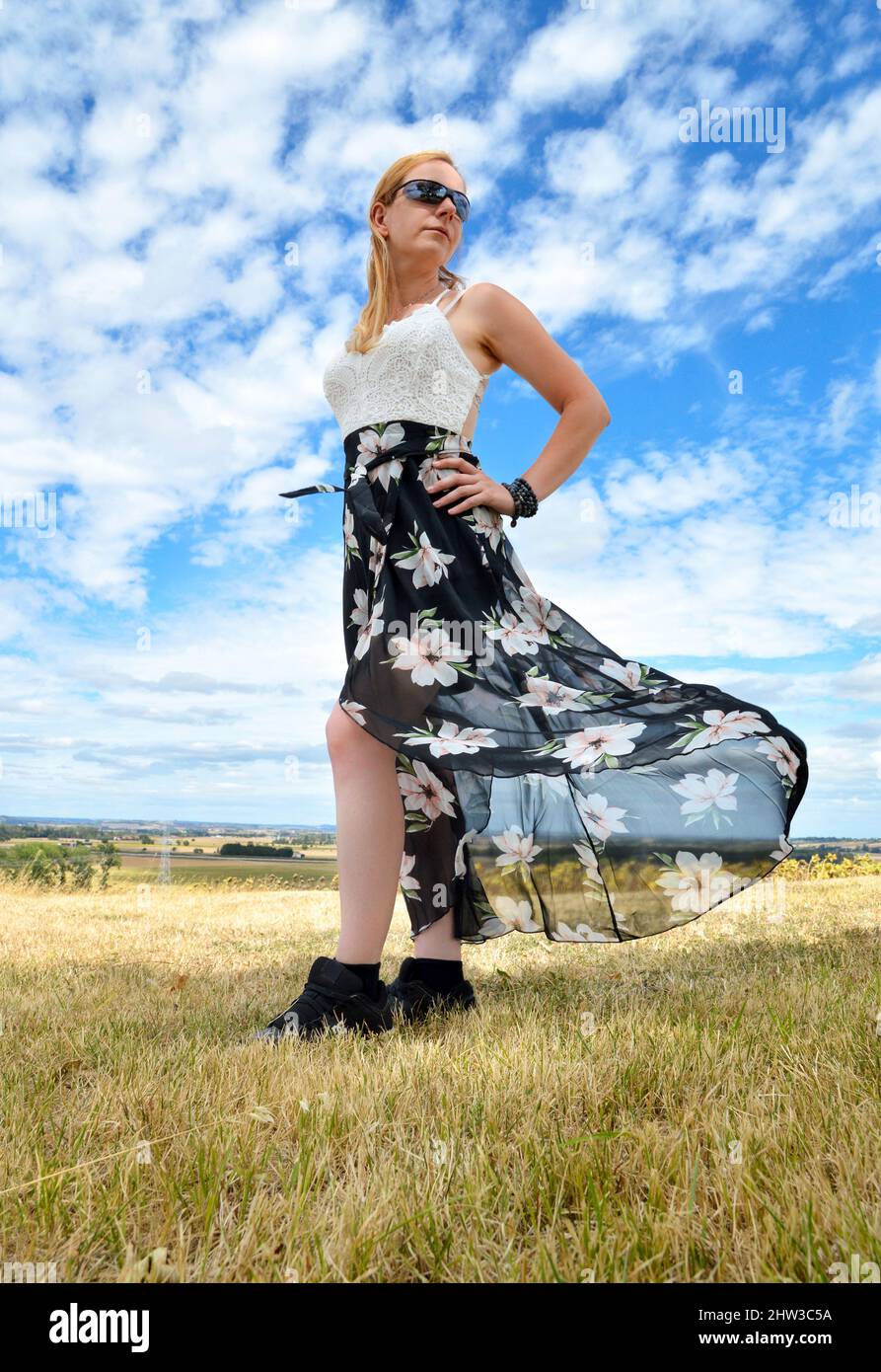 A beautiful blonde woman with a dress with flowers flying in the wind during spring Stock Photo