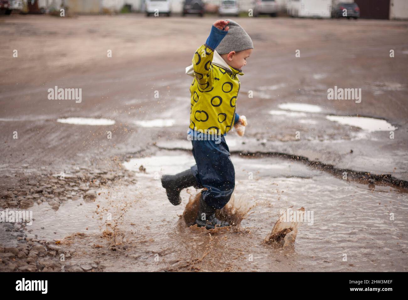 The child runs through the puddles. An awkward little boy. The boy enjoys life. Walk with a child on the street. Spring clothes on the child. A hypera Stock Photo
