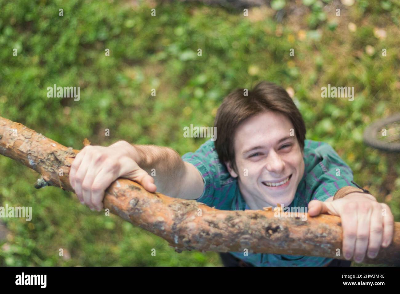 Guy hangs on tree branch. Behavior of child in man. Fun holiday. Man holds tight to canopy. Stock Photo
