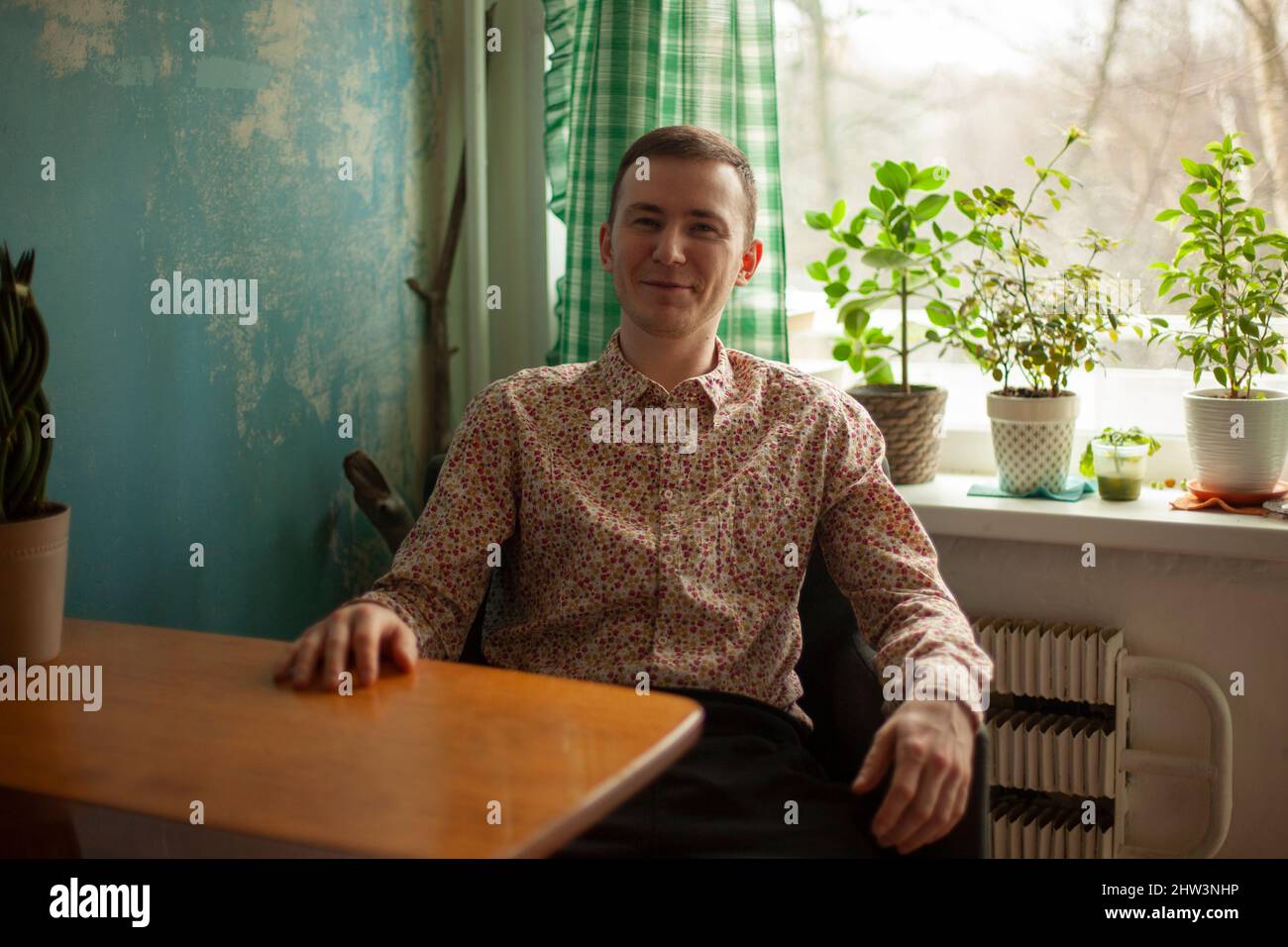 A man in Russia. A young man in the kitchen. A student in a shirt at home. A Russian guy is sitting in an old apartment. Natural light on a person's f Stock Photo