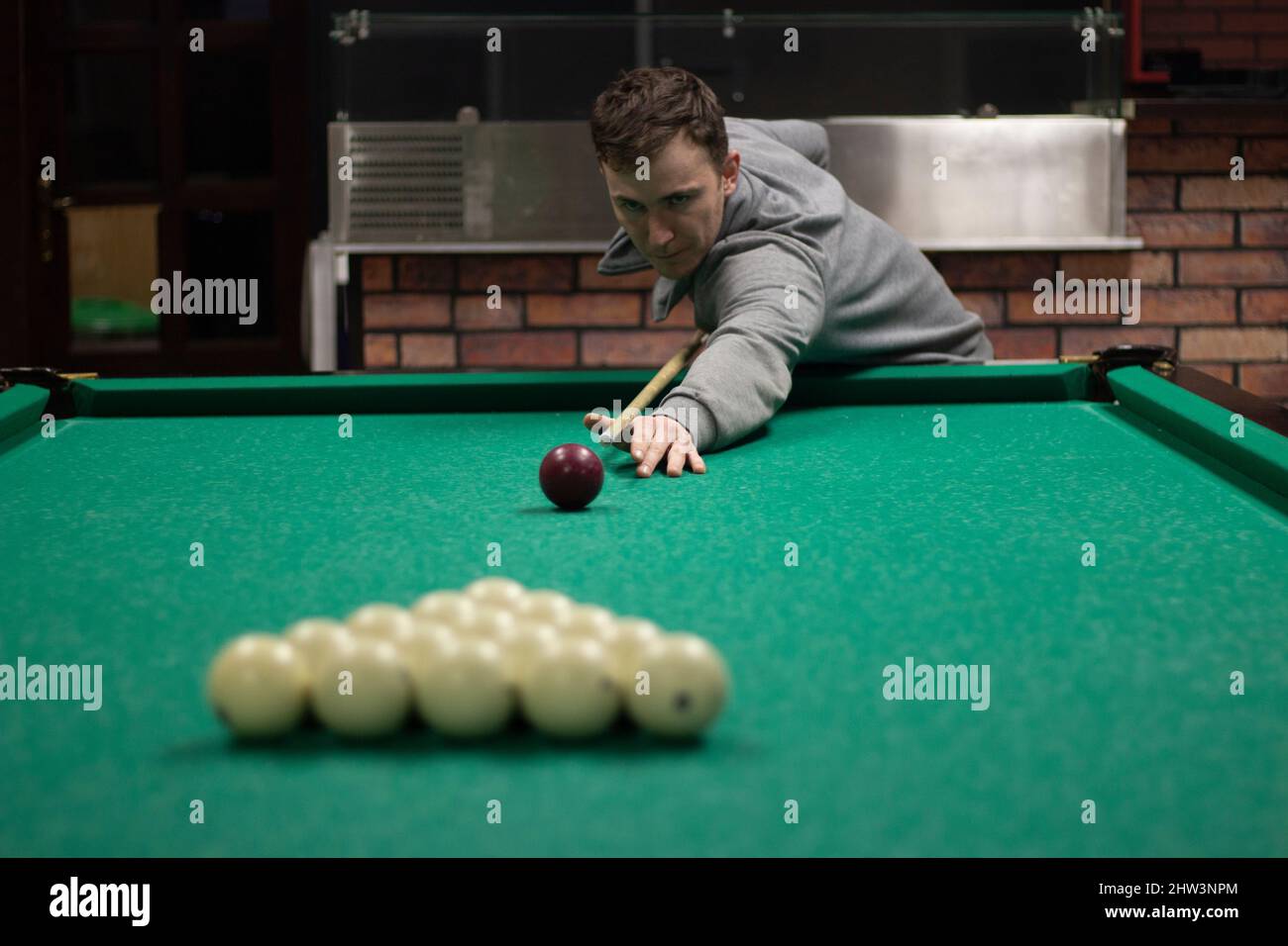 Guy plays billiards. Man hits balls. Student plays balls in bar