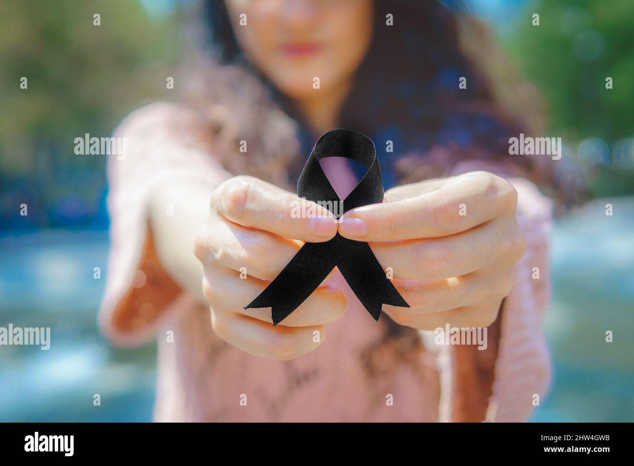 A woman wears an awareness ribbon. Black ribbon for melanoma cancer awareness. Stock Photo
