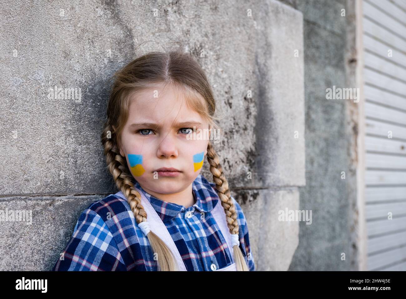 Portrait of a frightened child girl with painted flag on the cheek in yellow-blue colors of the Ukrainian flag. Peace and protection children concept Stock Photo