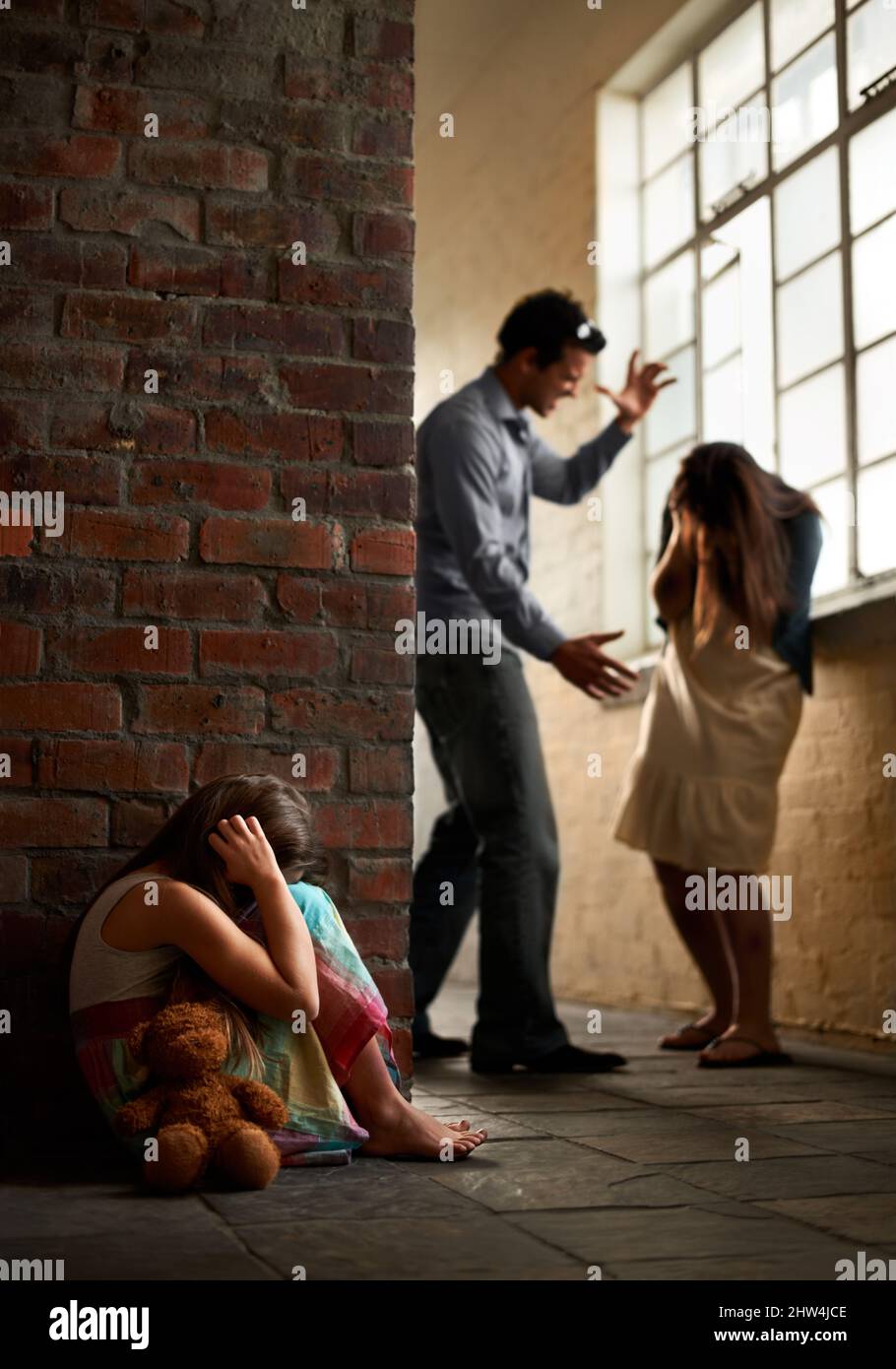 History of abuse. Little girl huddled over while her father abuses her mother nearby. Stock Photo