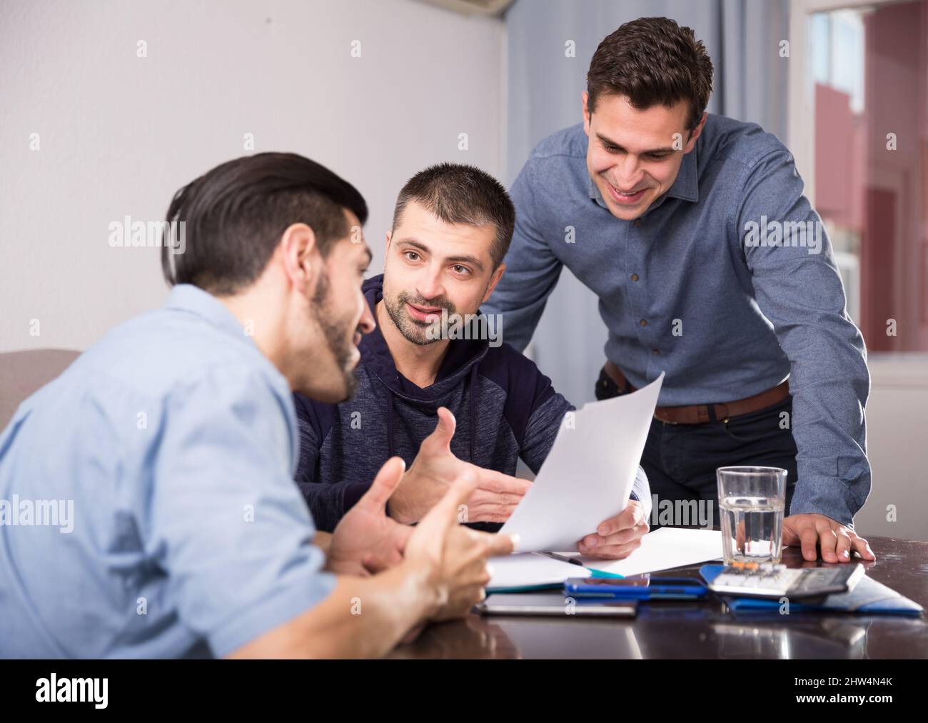 Three smiling men discussing papers at desk Stock Photo