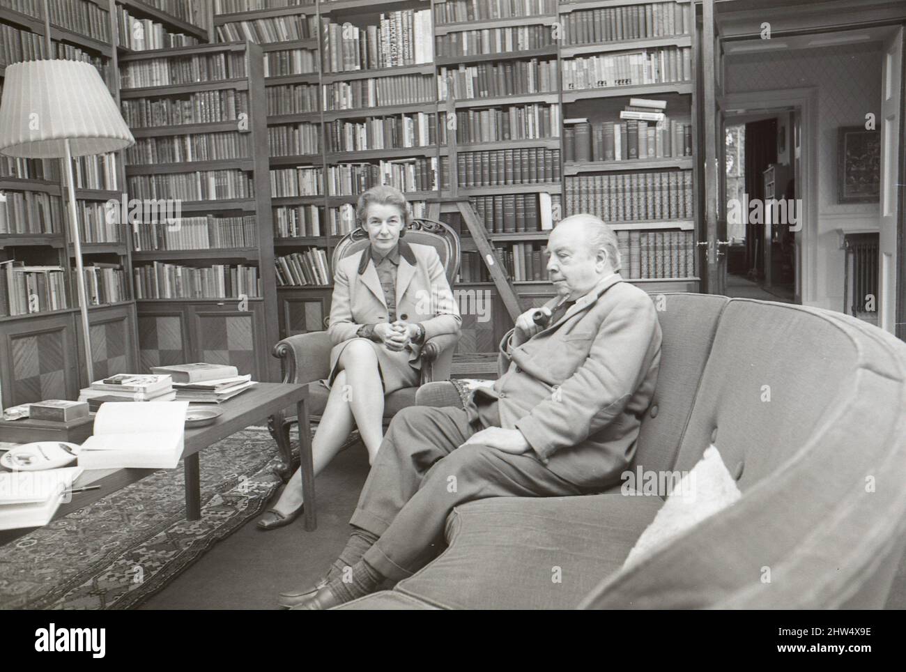 Novelist J. B. Priestley in the library of his home with his wife, Jacquetta Hawkes, at Kissing Tree House in the village of Alveston near Stratford.21st October 1968 Stock Photo