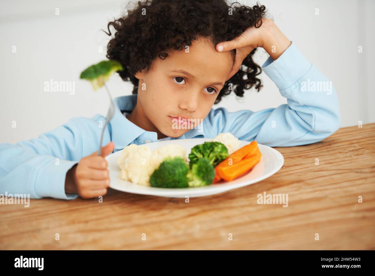 Broccoli again. Shot of an unimpressed-looking little boy sitting in front of a plate of vegetables. Stock Photo