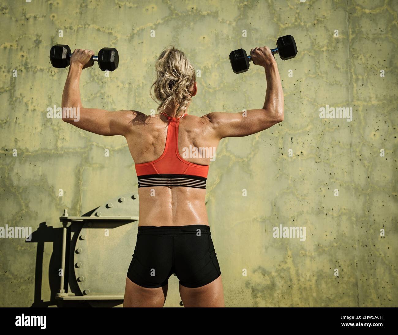 Rear view of athlete woman exercising with dumbbells Stock Photo