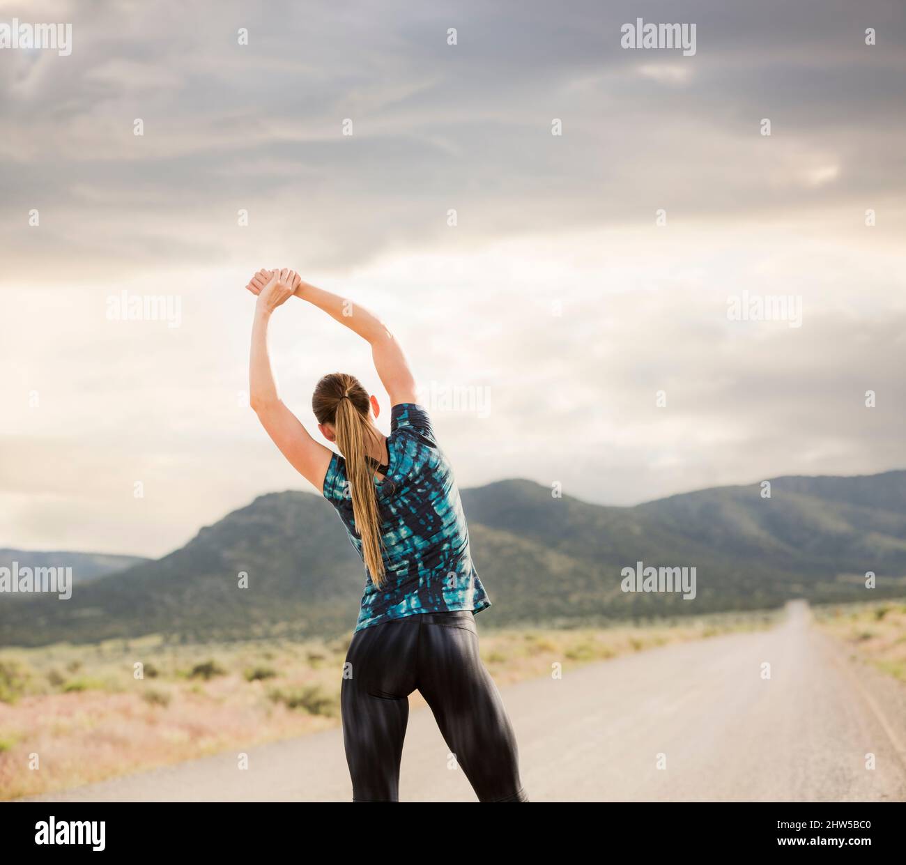 United States, Utah, Cedar Fort, Rear view of woman stretching on road in desert landscape Stock Photo