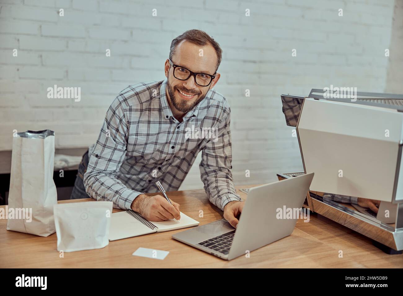 Cheerful man using laptop and taking notes in cafe Stock Photo