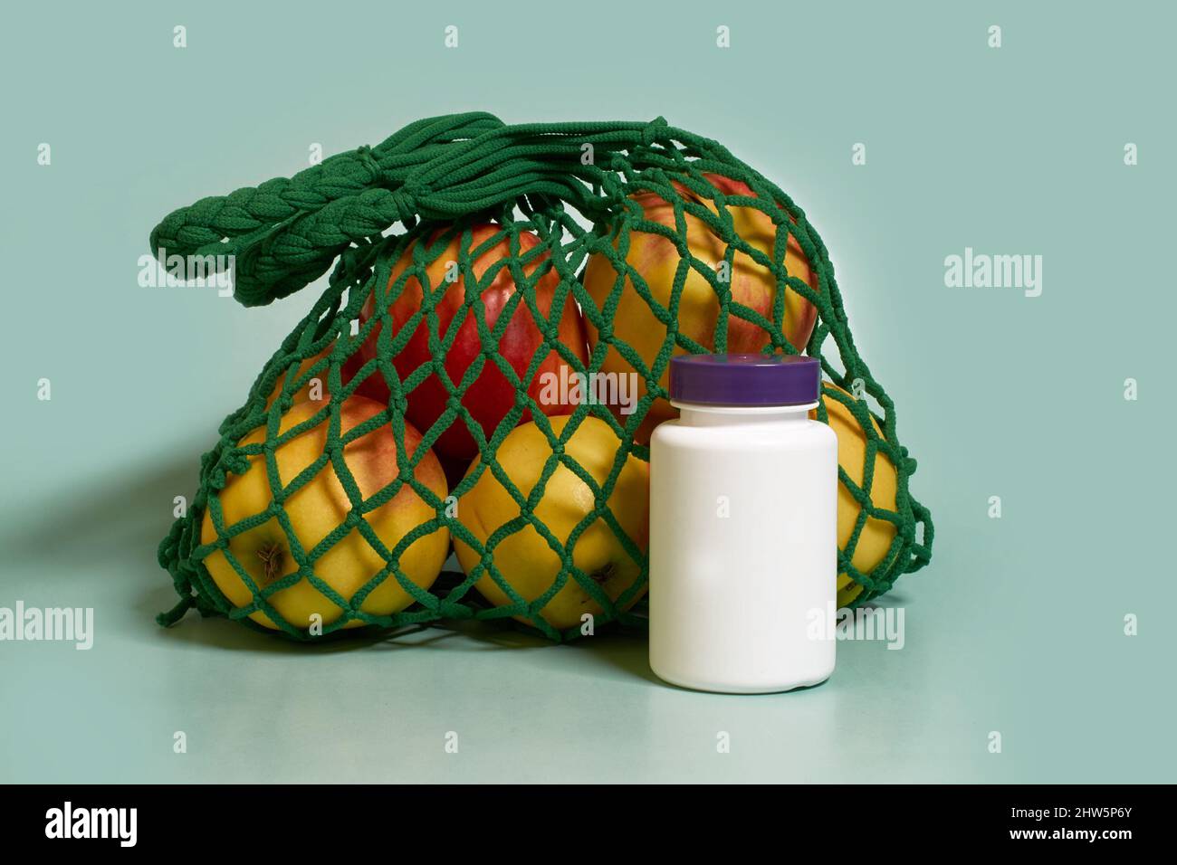 Mock up. A white plastic jar with a purple lid and mesh bag with apples Stock Photo