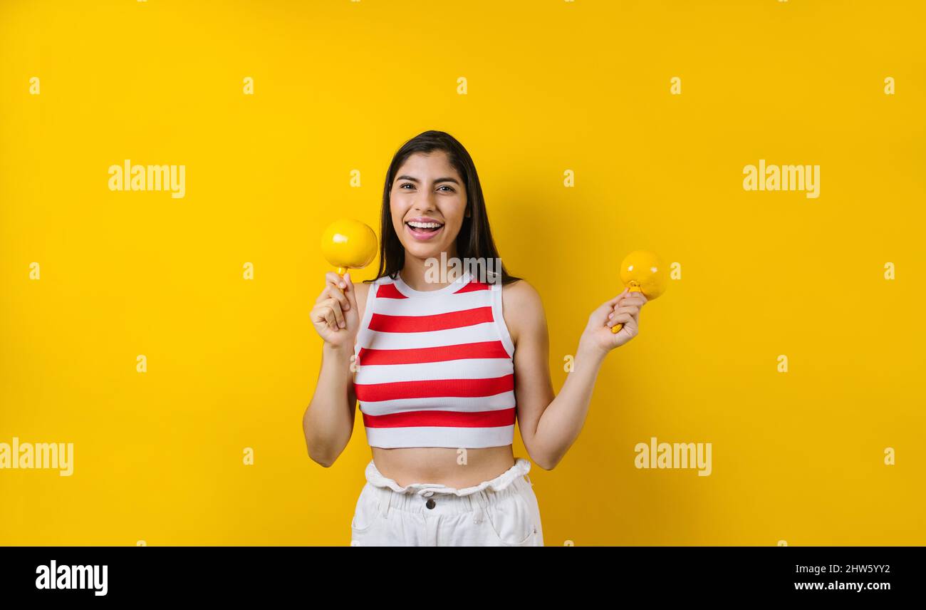 portrait of young latin woman holding mexican maracas or rattle on music concept and copy space on yellow background in Latin America Stock Photo