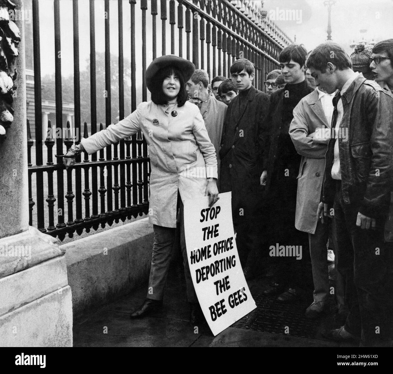 A young girl stands outside Buckingham Palace protesting against the proposed deportation of the two Australian members of the Bee Gees pop group by the Home Office as a crowd of boys gather round. August 1967. Stock Photo