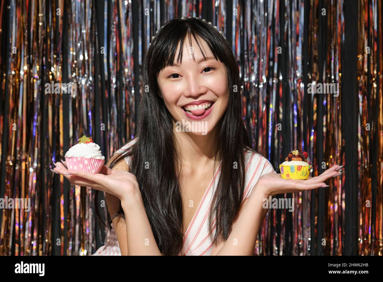 Young asian woman holds cupcakes in her hands over a party background. Stock Photo