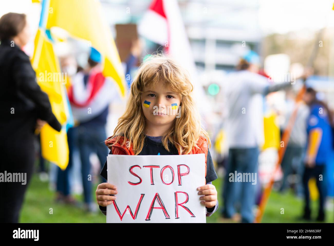 Portrait of child boy calls to Stop war in Ukraine, holding a poster with Stop the war message standing outdoor. Russian aggression. Child carries a Stock Photo