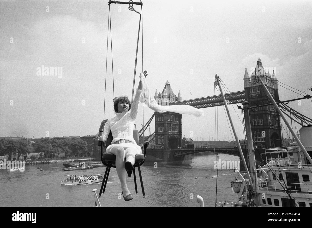 Advertising copywriter Vicki Morgan wanted publicity for an office chair designed by one of her clients, and Vicki's brainwave was that her chairs could be found anywhere - even 40ft high over London docks. So she arranged to have one slung out on a crane just above the Pool of London with a pretty woman sitting in it - Vicki decided to do the job herself. 10th June 1968 Stock Photo