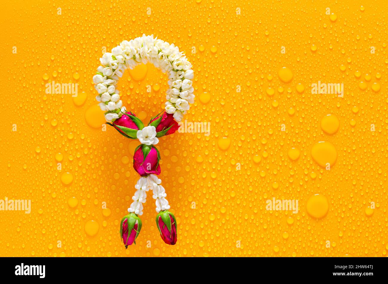 Jasmine garland puts on clear mirror that have wet yellow background below for Songkran festival concept. Stock Photo
