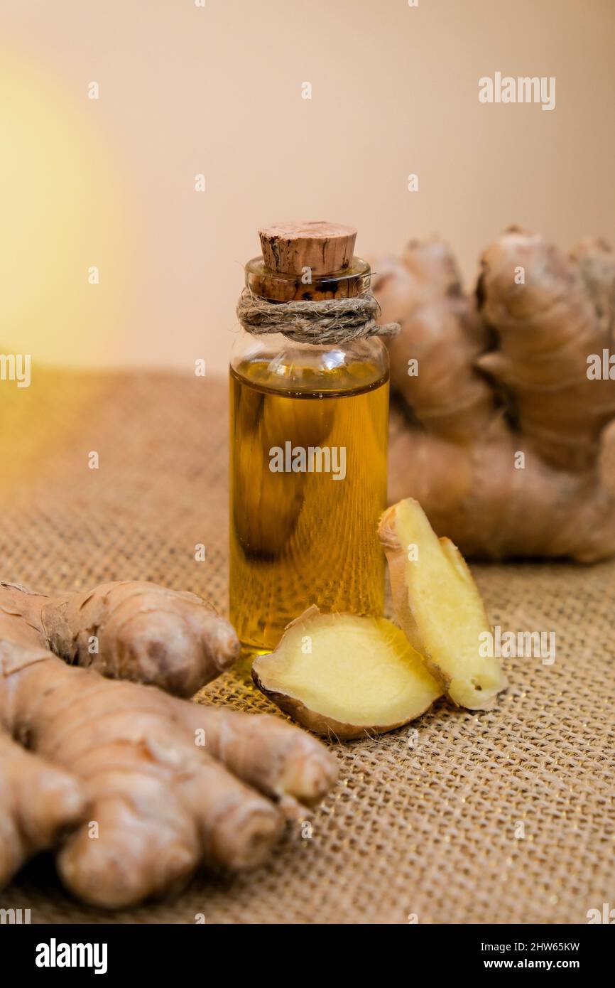 Glass bottle of essential ginger oil, ginger root on beige background