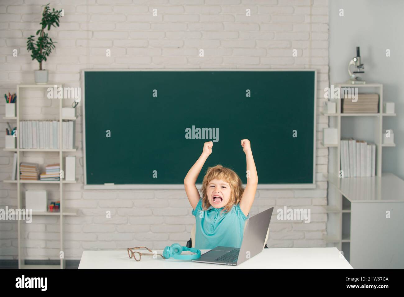 School child using digital pc laptop in class. Elementary school kid angry and sad. Pupil screaming shouting in classroom. Bad school boy. Stock Photo
