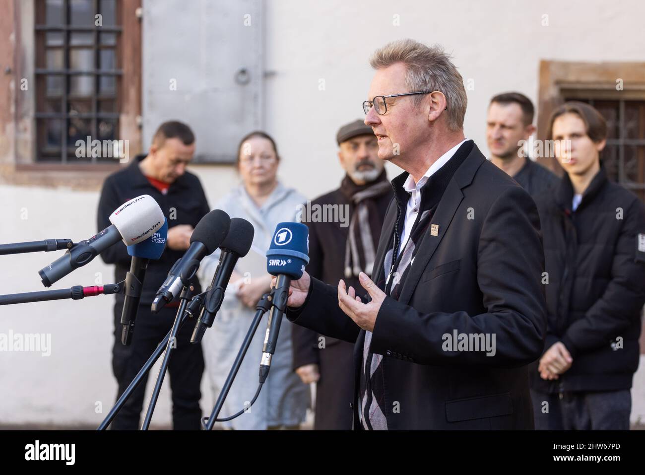 Freiburg, Germany. 03rd Mar, 2022. Ulrich von Kirchbach (SPD), First Mayor of Freiburg, stands in front of the microphones of media representatives and speaks while refugees from Ukraine stand behind him. 157 children and young people and around 30 caregivers had arrived in Freiburg on Sunday after a grueling flight from Ukraine and are now being housed on site. Credit: Philipp von Ditfurth/dpa/Alamy Live News Stock Photo