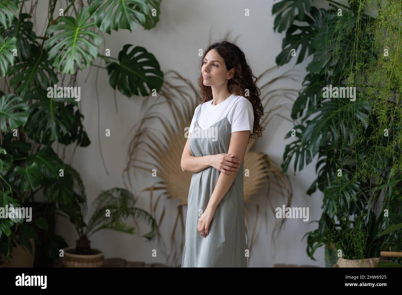 Young creative florist lady enjoy caring for houseplants in beautiful indoor garden with monstera Stock Photo