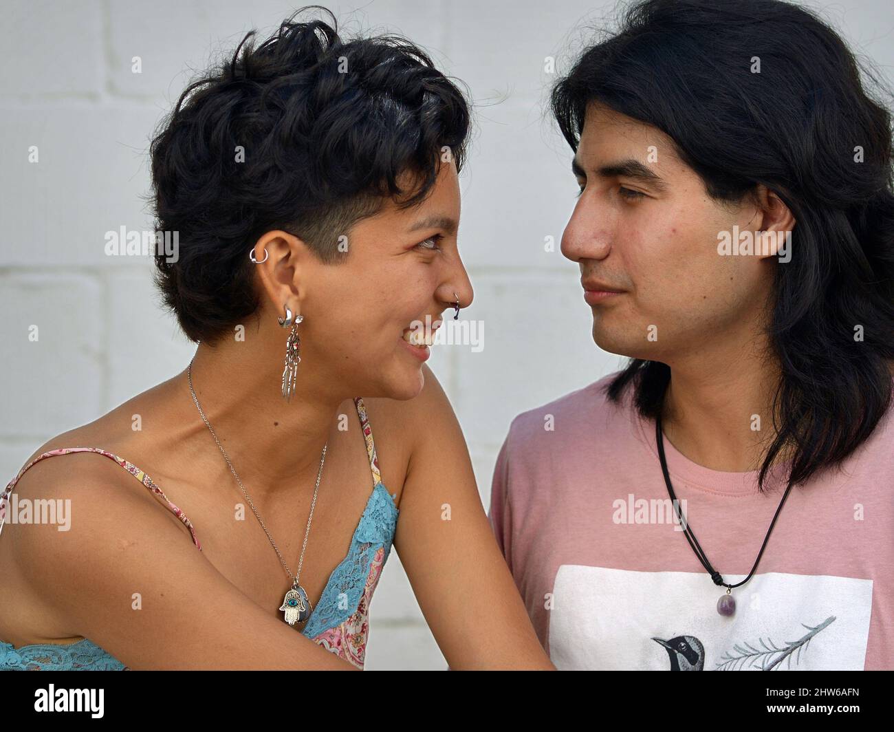 A beautiful smiling Mexican young Latina woman and a handsome serious Mexican young Latino man are in love and look into each other's eyes. Stock Photo
