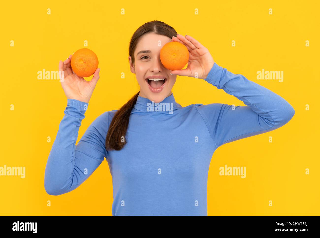 amazed young woman holding orange citrus fruit on yellow background, health Stock Photo