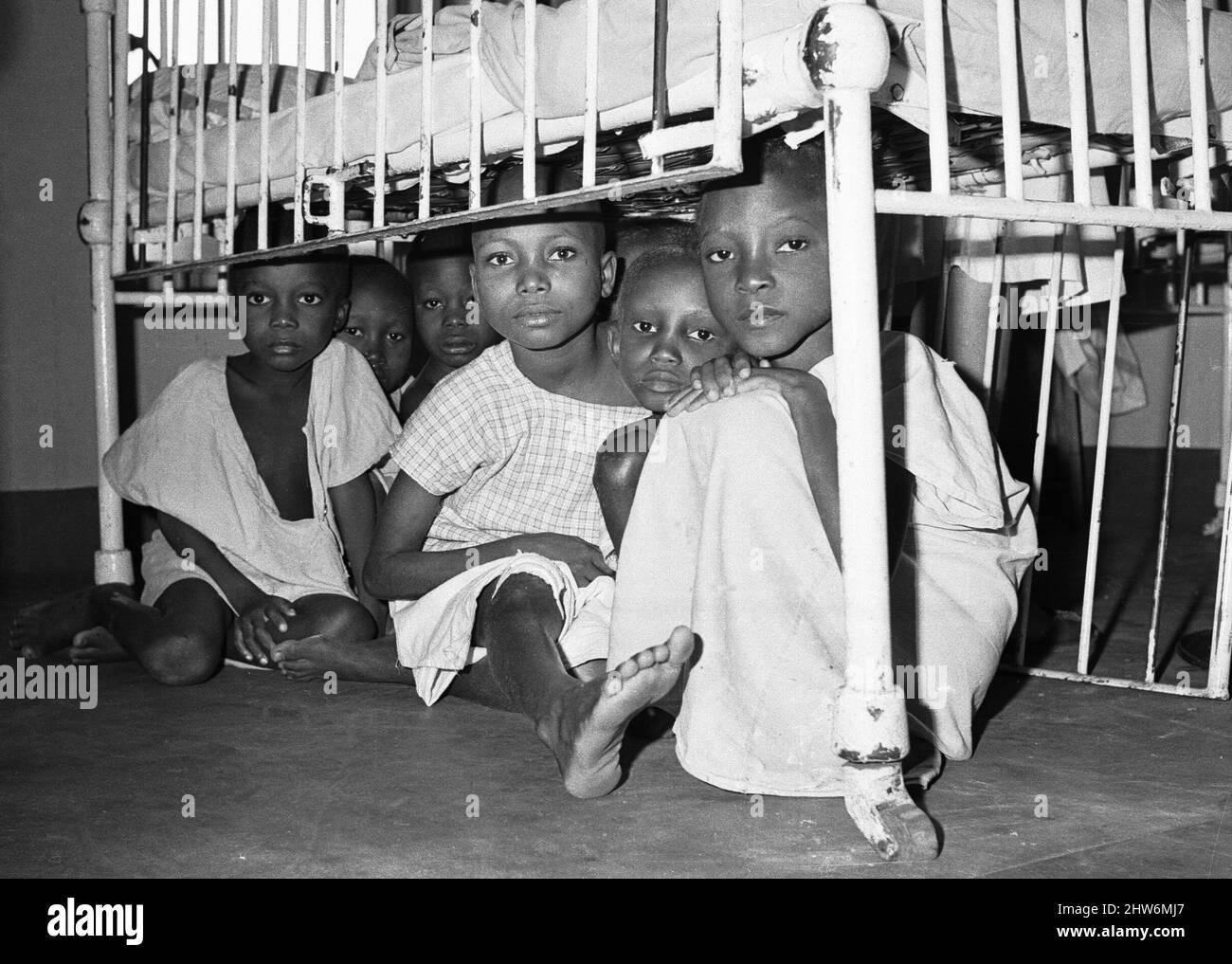 Children suffering from malnutrition hide under a cot during an air raid at Queen Elizabeth Hospital, Umuahia just one of the estimated one to two million victims of the Biafran War. 11th June 1968The Nigerian Civil War, also known as the Biafran War endured for two and a half years, from  6 July 1967 to 15 January 1970, and was fought to counter the secession of Biafra from Nigeria. The indigenous Igbo people of Biafra felt they could no longer co-exist with the Northern-dominated federal government following independence from Great Britain. Political, economic, ethnic, cultural and religious Stock Photo