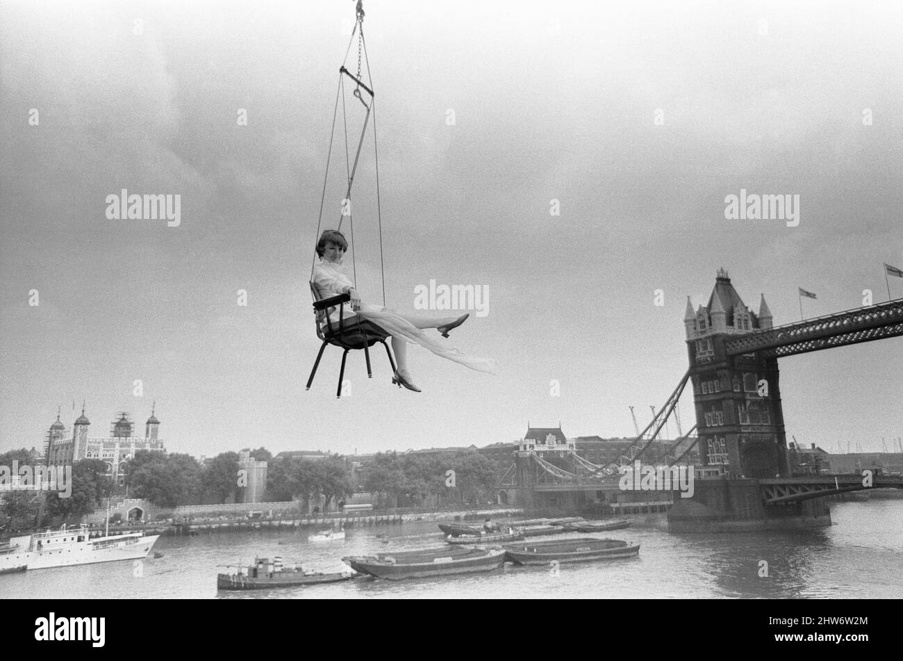Advertising copywriter Vicki Morgan wanted publicity for an office chair designed by one of her clients, and Vicki's brainwave was that her chairs could be found anywhere - even 40ft high over London docks. So she arranged to have one slung out on a crane just above the Pool of London with a pretty woman sitting in it - Vicki decided to do the job herself. 10th June 1968 Stock Photo