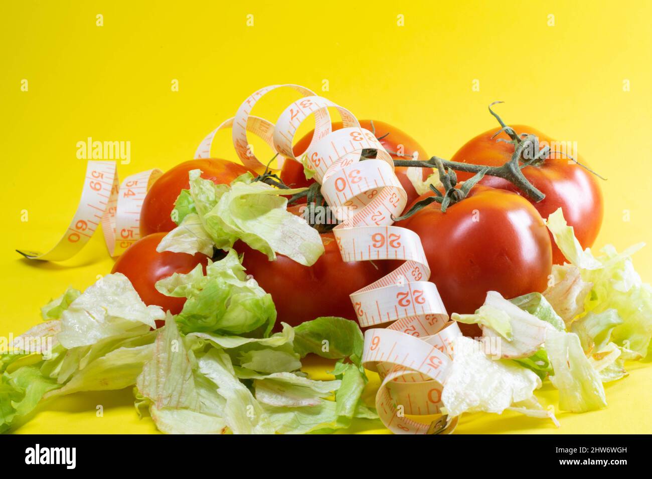 Closeup shot of the tomatoes, letus and tape measure tailor on the yellow background Stock Photo