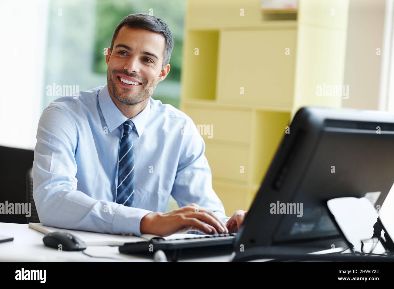 Working with a smile. A smiling young businessman sitting at his desk ...