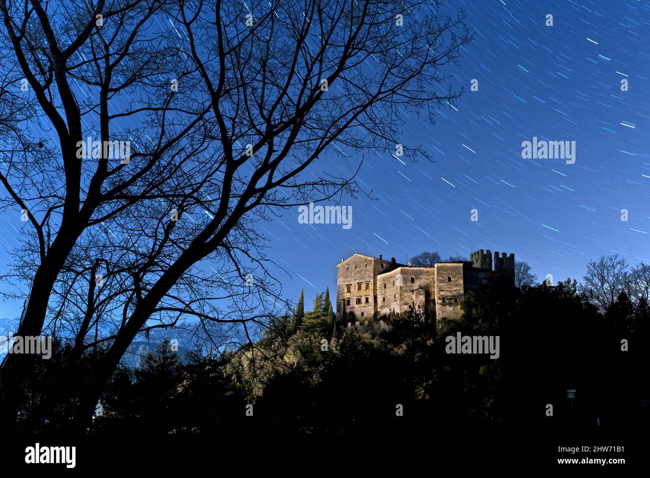 Skeletal trees frame Madruzzo Castle on a spooky night. Madruzzo, Trento province, Trentino Alto-Adige, Italy, Europe. Stock Photo