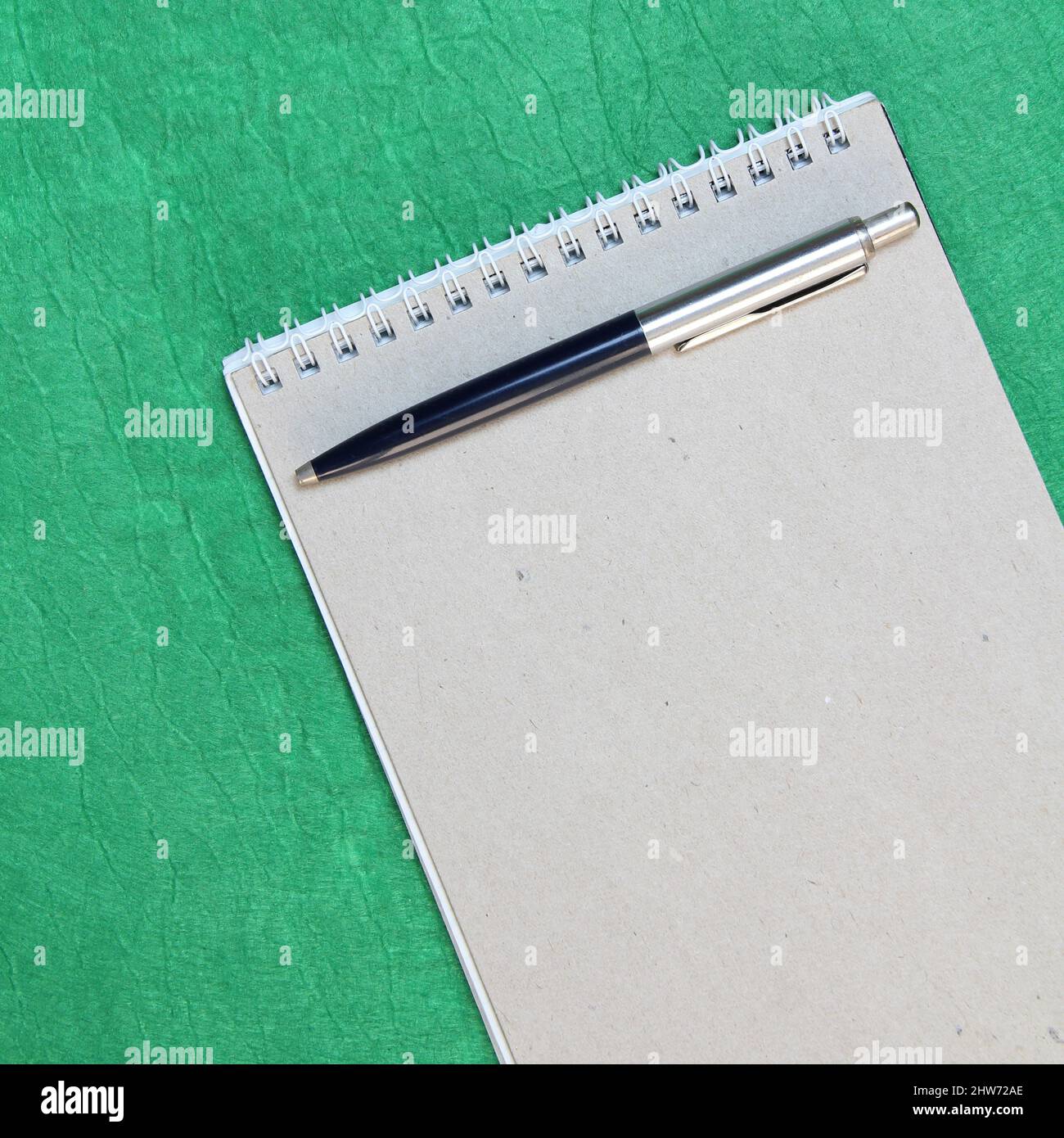 White and gray notepad sheet with spiral with pen against the background of green fabric. Concept of analysis, study, attentive work. Stock photo with empty place for your text and design. Square image shape. Stock Photo