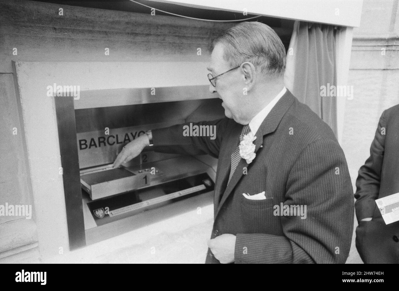 The Worlds First ATM, Cash Machine is unveiled at Barclays Bank, in Enfield, Middlesex, just North of London. 27th June 1967. Picture shows a customer using the machine.  Barclays ATM, 27th June 1967. Sir Thomas Bland, Deputy Chairman of Barclays Bank, unveils a robot cashier that dispenses cash at any time of the day or night. Designed and developed jointly with De la rue Instruments & the banks Management Services Department, the BarclayCash machine is installed at the Enfield branch. Actor, Reg Varney took time off from filming for the TV series 'Beggar Your Neighbour' at Northwood to be th Stock Photo